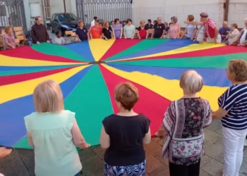 Partecipanti riuniti attorno a un grande paracadute colorato durante un momento di animazione in piazza Carmine, nell'ambito della festa della Madonna del Carmine a Ragusa.