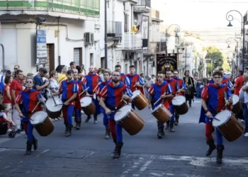 I Tamburi di Giarratana in costume medievale sfilano durante il MeMuFest lungo una strada del centro storico, accompagnati dal pubblico