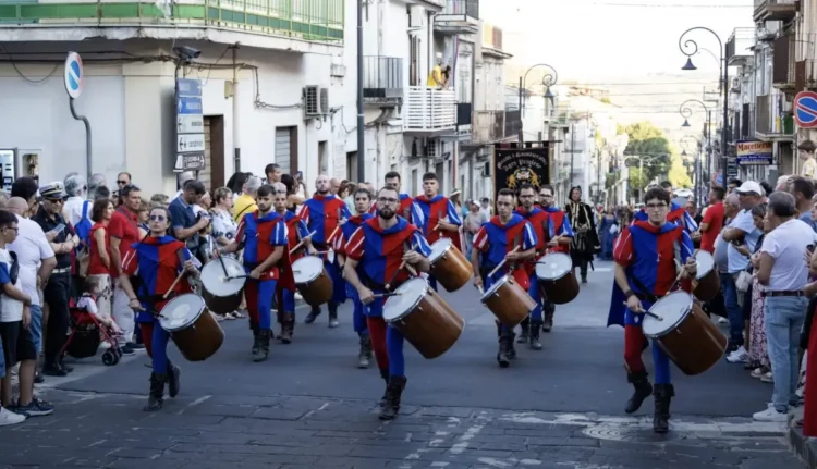 I Tamburi di Giarratana in costume medievale sfilano durante il MeMuFest lungo una strada del centro storico, accompagnati dal pubblico