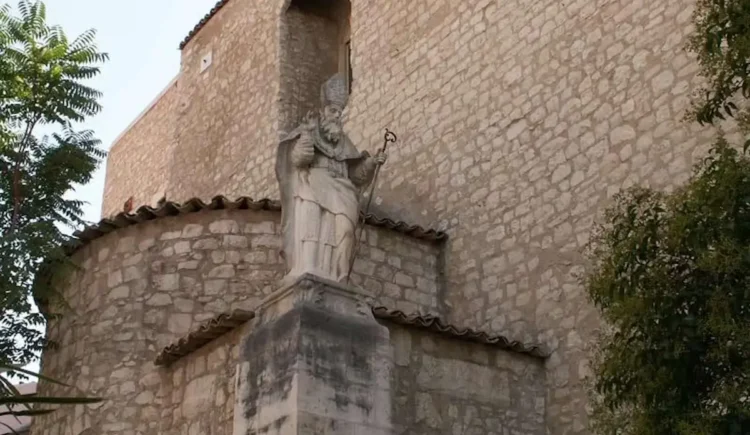 La statua di San Biagio collocata davanti alla chiesa dedicata al patrono di Comiso, con la facciata in pietra dell'edificio religioso sullo sfondo