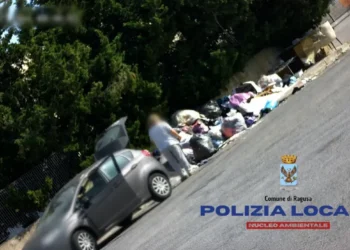 Persona accanto a un cumulo di rifiuti abbandonati lungo una strada a Ragusa durante un controllo della Polizia Locale