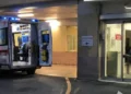 Ambulanza parcheggiata all'ingresso del pronto soccorso di un ospedale con le porte posteriori aperte e l'area di accettazione illuminata.