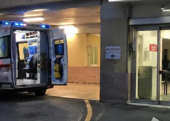 Ambulanza parcheggiata all'ingresso del pronto soccorso di un ospedale con le porte posteriori aperte e l'area di accettazione illuminata.