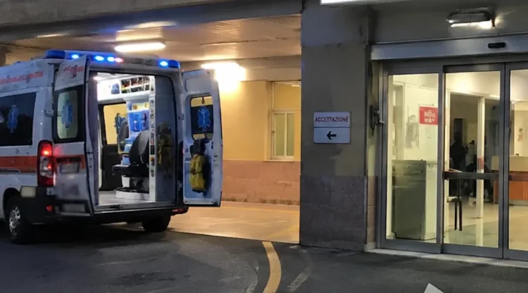 Ambulanza parcheggiata all'ingresso del pronto soccorso di un ospedale con le porte posteriori aperte e l'area di accettazione illuminata.