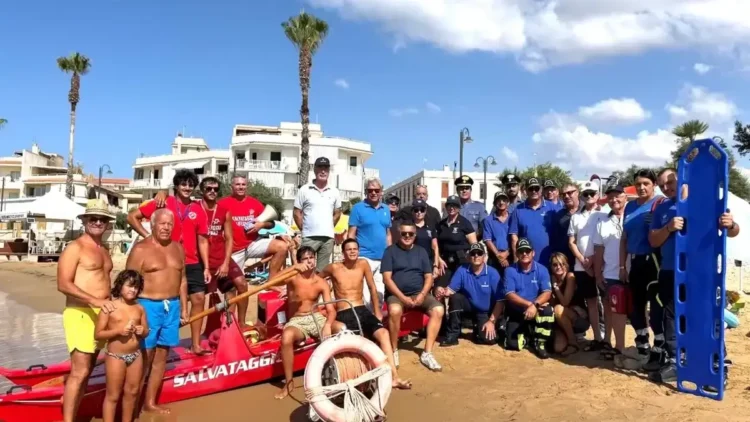 Bagnini, carabinieri e volontari della protezione civile in posa sulla spiaggia accanto a un pattino di salvataggio