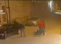 Fermo immagine da telecamera di sorveglianza: due uomini aggrediscono una persona a terra in una strada notturna