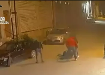Fermo immagine da telecamera di sorveglianza: due uomini aggrediscono una persona a terra in una strada notturna