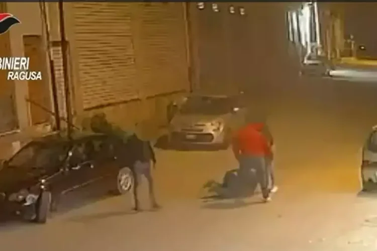 Fermo immagine da telecamera di sorveglianza: due uomini aggrediscono una persona a terra in una strada notturna