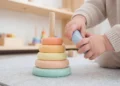 Bambino piccolo che gioca con una piramide di anelli colorati in legno sul pavimento di un asilo nido
