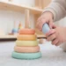 Bambino piccolo che gioca con una piramide di anelli colorati in legno sul pavimento di un asilo nido
