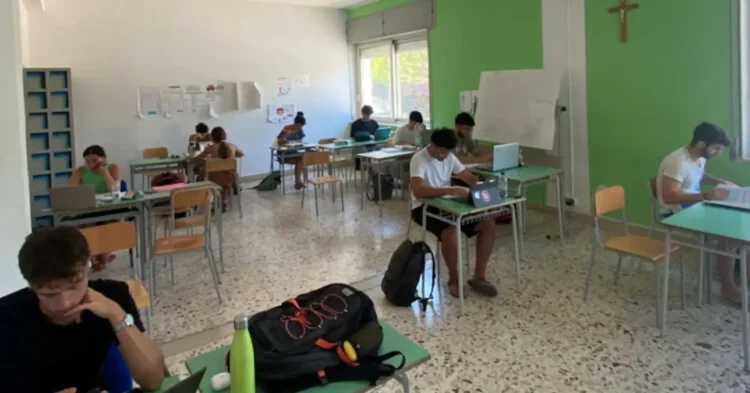 Studenti impegnati nello studio all'interno dell'aula studio estiva di Marina di Ragusa, con postazioni individuali e computer portatili.