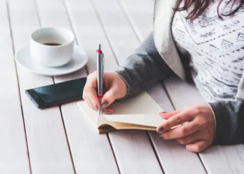 Giovane lavoratrice scrive su un taccuino accanto a uno smartphone e a una tazza di caffè, immagine utilizzata per illustrare il bonus giovani under 35 dell'Inps.