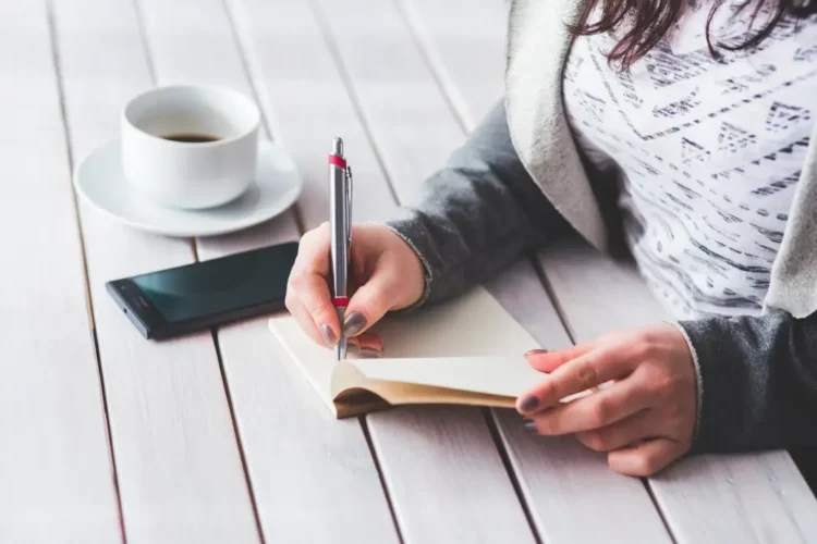 Giovane lavoratrice scrive su un taccuino accanto a uno smartphone e a una tazza di caffè, immagine utilizzata per illustrare il bonus giovani under 35 dell'Inps.