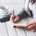 Giovane lavoratrice scrive su un taccuino accanto a uno smartphone e a una tazza di caffè, immagine utilizzata per illustrare il bonus giovani under 35 dell'Inps.