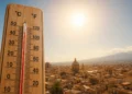 Primo piano di un termometro con temperature elevate davanti al panorama di una città siciliana illuminata dal sole, a rappresentare l'ondata di caldo estremo