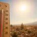 Primo piano di un termometro con temperature elevate davanti al panorama di una città siciliana illuminata dal sole, a rappresentare l'ondata di caldo estremo