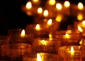 Primo piano di diverse candele votive accese, con fiamme che illuminano un ambiente buio, simbolo di lutto, commemorazione e raccoglimento.
