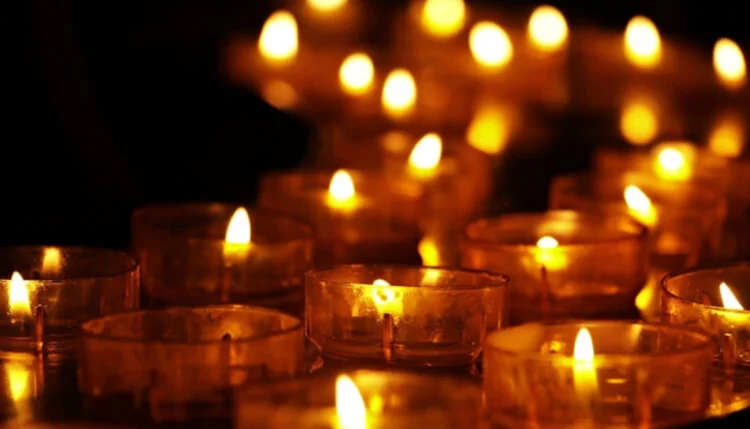 Primo piano di diverse candele votive accese, con fiamme che illuminano un ambiente buio, simbolo di lutto, commemorazione e raccoglimento.