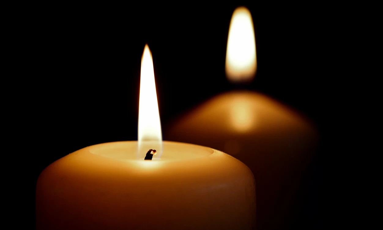 Primo piano di una candela accesa con una seconda candela sfocata sullo sfondo, immagine simbolica utilizzata per rappresentare lutto, ricordo e cordoglio.