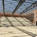 Interno del nuovo palazzetto dello sport di Comiso in costruzione, con gradinate in cemento, struttura portante della copertura e operai presenti durante il sopralluogo dell'assessore ai Lavori pubblici.