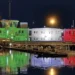 La sede della Capitaneria di Porto di Pozzallo illuminata con i colori del tricolore italiano riflessi sul mare di notte.