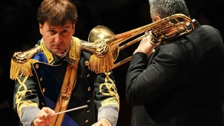 Maestro direttore della Banda musicale della Guardia di Finanza durante un'esibizione con un musicista al trombone.