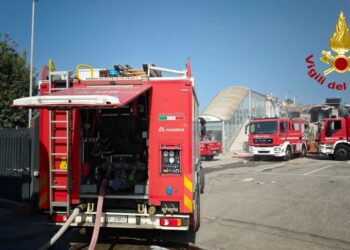 Tre autopompe dei Vigili del fuoco schierate in un piazzale davanti a un edificio parzialmente crollato