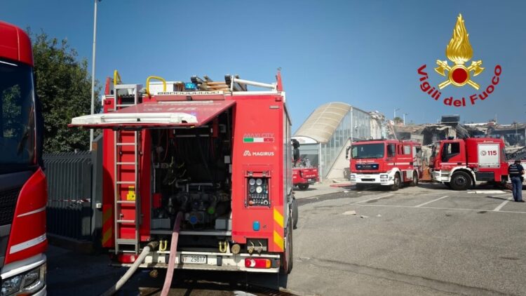 Tre autopompe dei Vigili del fuoco schierate in un piazzale davanti a un edificio parzialmente crollato