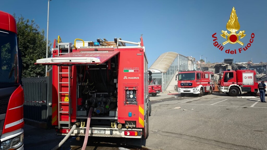 Tre autopompe dei Vigili del fuoco schierate in un piazzale davanti a un edificio parzialmente crollato