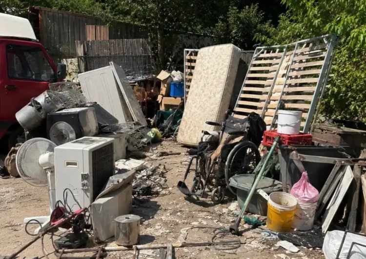 Rifiuti ingombranti accumulati in un'area all'aperto: materassi, elettrodomestici, una sedia a rotelle, legname e rottami metallici