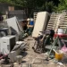 Rifiuti ingombranti accumulati in un'area all'aperto: materassi, elettrodomestici, una sedia a rotelle, legname e rottami metallici