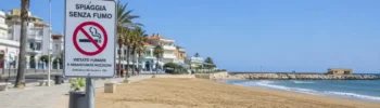 Cartello di divieto di fumo sulla spiaggia di Marina di Ragusa con il litorale, il lungomare e il mare sullo sfondo