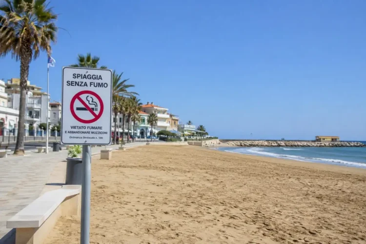 Cartello di divieto di fumo sulla spiaggia di Marina di Ragusa con il litorale, il lungomare e il mare sullo sfondo