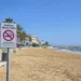 Cartello di divieto di fumo sulla spiaggia di Marina di Ragusa con il litorale, il lungomare e il mare sullo sfondo