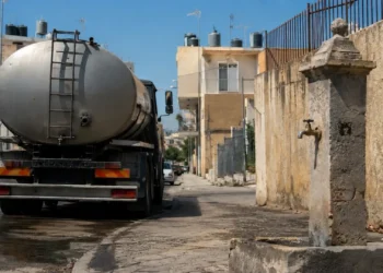 Autobotte in una strada di Vittoria durante l'emergenza idrica, con fontana pubblica e serbatoi sugli edifici.