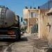 Autobotte in una strada di Vittoria durante l'emergenza idrica, con fontana pubblica e serbatoi sugli edifici.
