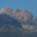 Colonna di cenere e fumo grigio dal cratere Voragine dell'Etna, con il versante innevato sullo sfondo e cielo sereno