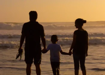 Una famiglia con un bambino osserva il mare al tramonto, tenendosi per mano sulla battigia. Immagine simbolica dedicata al sostegno economico per le famiglie e all'assegno unico.