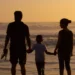 Una famiglia con un bambino osserva il mare al tramonto, tenendosi per mano sulla battigia. Immagine simbolica dedicata al sostegno economico per le famiglie e all'assegno unico.