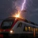 Un treno passeggeri viene colpito da un fulmine durante un forte temporale notturno, con pioggia intensa e scintille sul tetto del convoglio