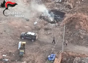 Veduta aerea dell'intervento dei Carabinieri in un'area di Scoglitti interessata da un rogo di rifiuti speciali, con fumo visibile e mezzi dell'Arma sul posto.