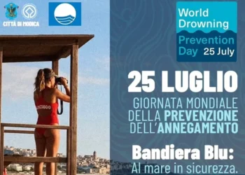 Locandina del World Drowning Prevention Day del 25 luglio a Marina di Modica con una bagnina in torretta di avvistamento e il richiamo alla Giornata mondiale della prevenzione dell'annegamento promossa nei Comuni Bandiera Blu.