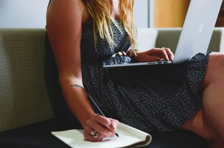 Giovane lavoratrice utilizza un computer portatile mentre prende appunti, immagine di repertorio sul bonus giovani 2026 per la stabilizzazione dei contratti di lavoro