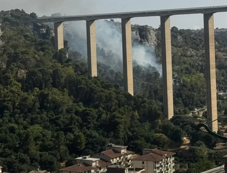 Incendio boschivo sotto il ponte Guerrieri, in via Fiumara tra Modica e Scicli, con colonne di fumo che si alzano dalla vegetazione mentre sono in corso le operazioni di spegnimento