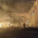 Un vigile del fuoco contrasta le fiamme nel deposito della Repack srl sulla SP 85, con la struttura metallica visibilmente danneggiata