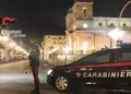 Pattuglia dei Carabinieri di Catania di notte in una piazza cittadina, militare in servizio accanto all'auto di pattuglia