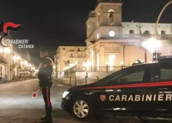 Pattuglia dei Carabinieri di Catania di notte in una piazza cittadina, militare in servizio accanto all'auto di pattuglia