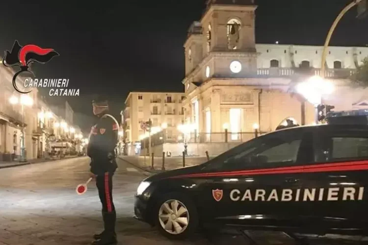 Pattuglia dei Carabinieri di Catania di notte in una piazza cittadina, militare in servizio accanto all'auto di pattuglia