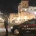Pattuglia dei Carabinieri di Catania di notte in una piazza cittadina, militare in servizio accanto all'auto di pattuglia
