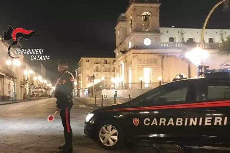 Pattuglia dei Carabinieri di Catania di notte in una piazza cittadina, militare in servizio accanto all'auto di pattuglia